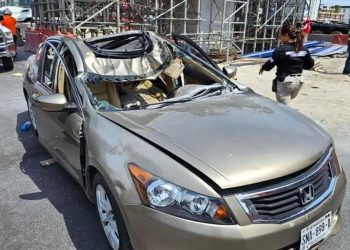 Gold Honda Sedan with Severely Damaged Roof and Shattered Side Windows at an Accident Scene, Construction Scaffolding in the Background. - Salud Regia