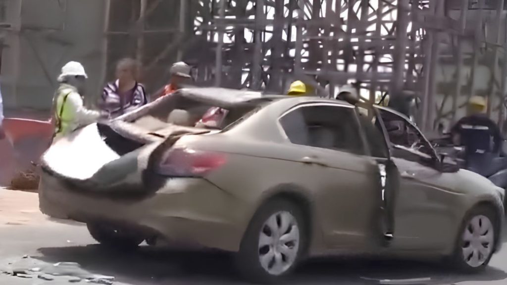 Beige Sedan Heavily Damaged with a Crushed Roof and Open Door, Responders in Helmets and Safety Vests Nearby at a Construction Site Backdrop. - Salud Regia