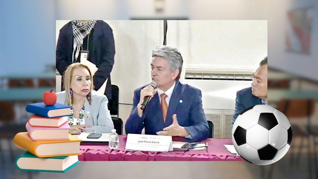 Panel Discussion: Man in a Blue Suit Speaks into a Microphone Beside a Seated Woman at a Table, with a Stack of Books on the Left and a Large Soccer Ball on the Right Behind Them. - Salud Regia
