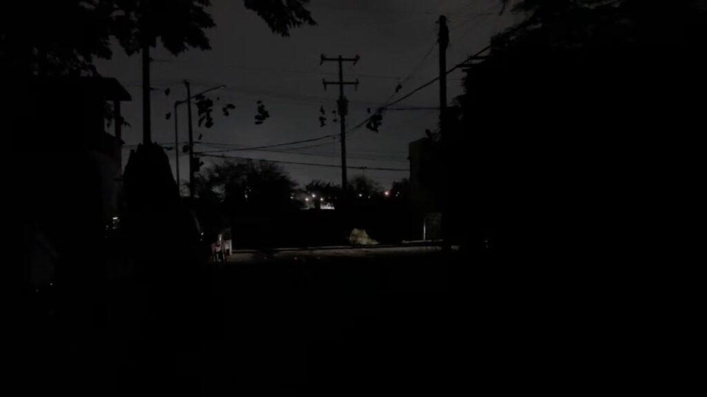 Dark Urban Street at Night with Silhouettes of Utility Poles and Tangled Power Lines, Distant Lights Glowing on the Horizon Behind Trees Stillness in the Foreground. - Salud Regia