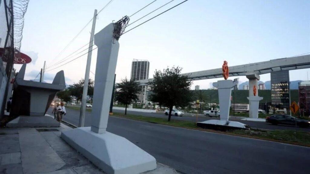 Puente-peatonal-constitución-tótems-naranjas-publicidad - Salud Regia Urban Street Scene with Large White Decorative Columns Along the Road, Barbed Wire Fence on the Left, and a Pedestrian Nearby. - Salud Regia