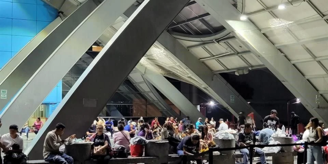 Duermen-en-la-calle-afuera-del-hospital-materno-infantil - Salud Regia Crowded Indoor Waiting Area with People Sitting at Tables and Benches Beneath Large Diagonal Steel Beams. - Salud Regia